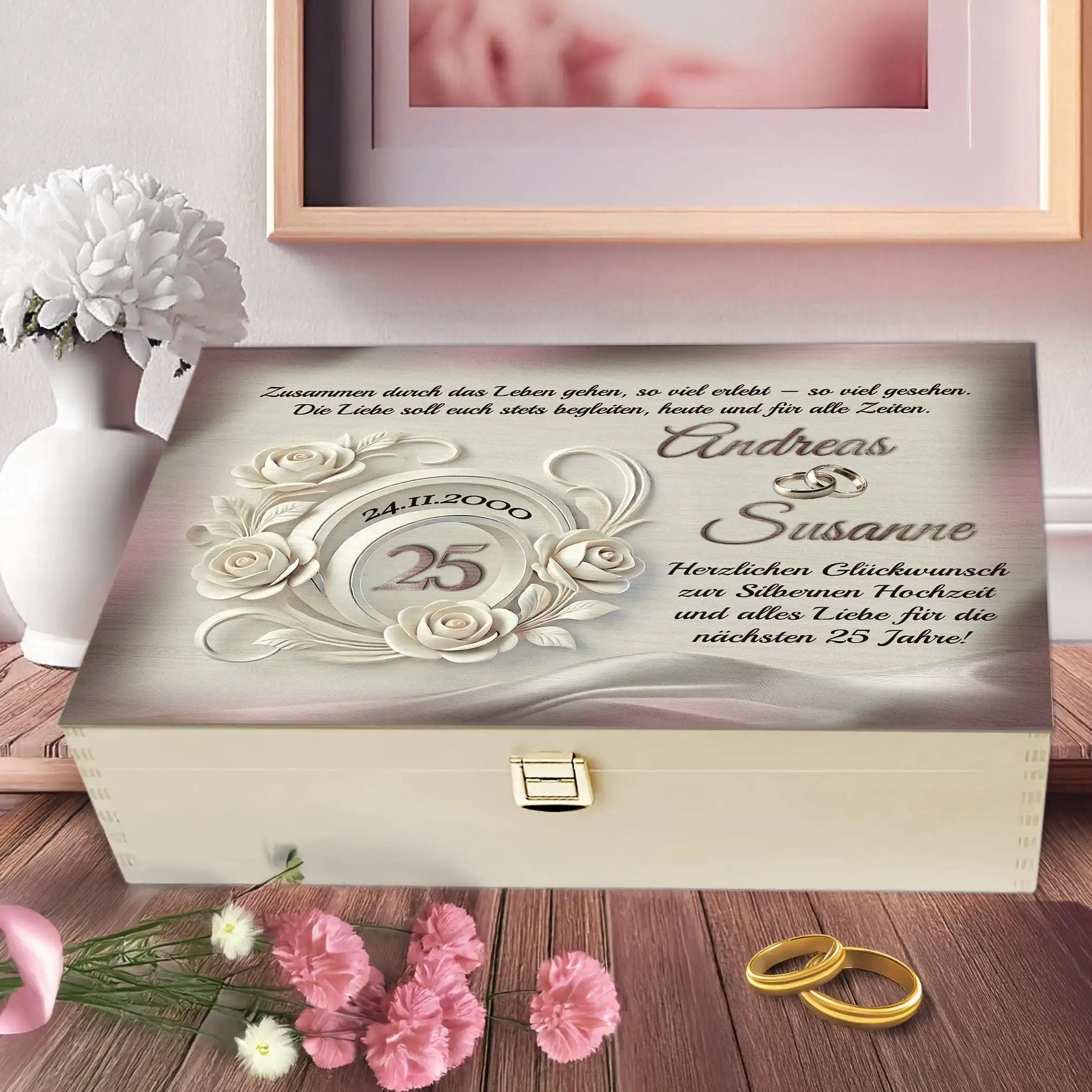 Holzbox zur Silberhochzeit mit gravierten Namen, Blumenmotiv und goldenen Ringen auf Tisch