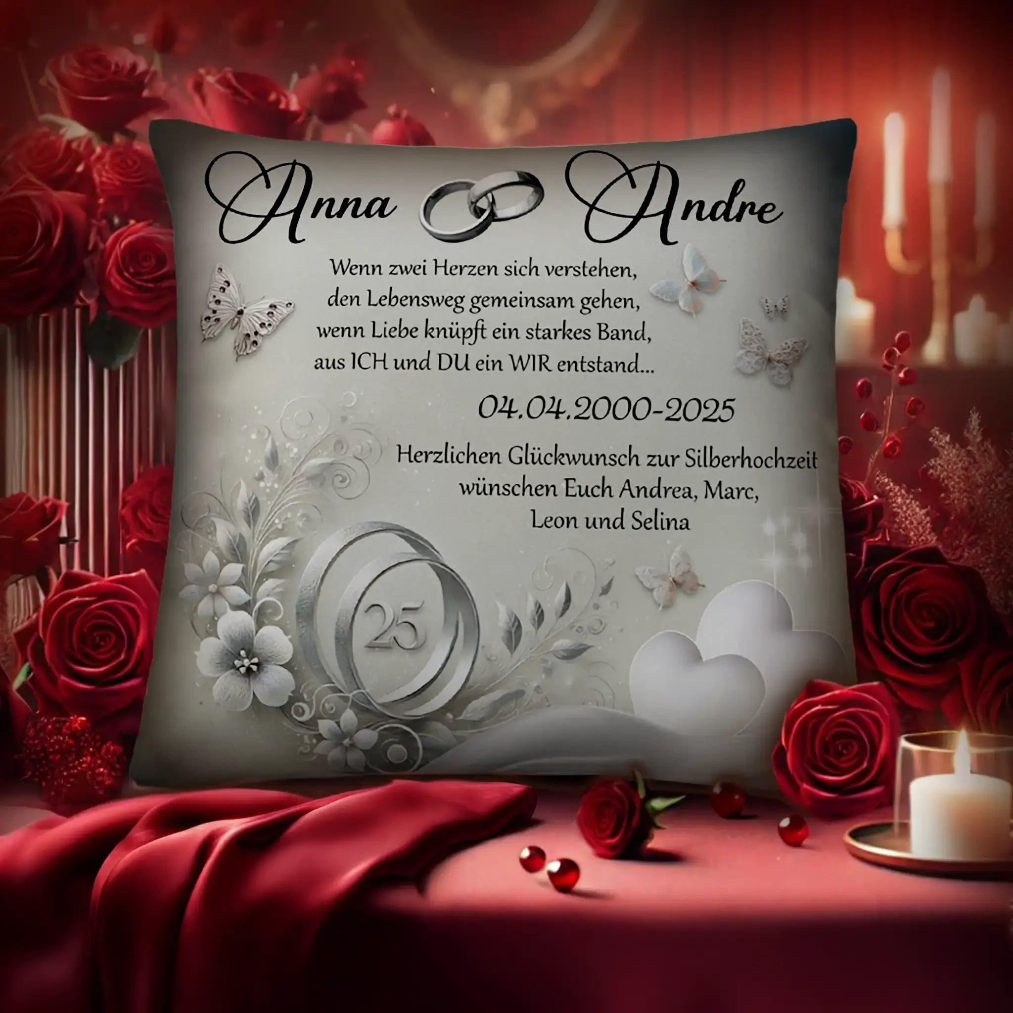 Zierkissen zur Silberhochzeit mit Spruch, Silberringen und floralen Motiven, umgeben von roten Rosen und Kerzen.