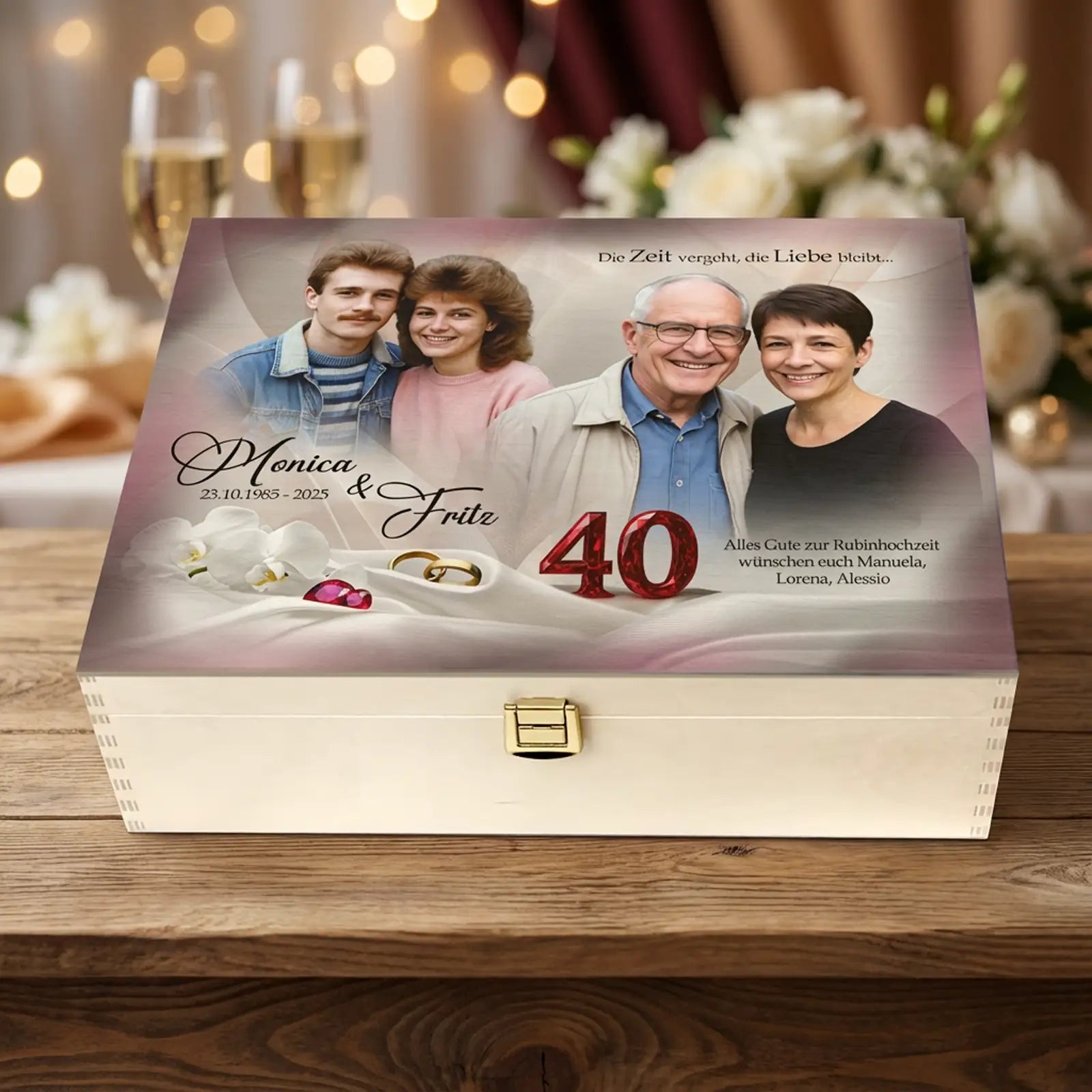 Personalisierte helle Holzbox zur Rubinhochzeit (40 Jahre) mit Fotodruck auf dem Deckel. Auf der Box sind zwei Fotos eines Ehepaares aus jungen und späteren Jahren zu sehen, dazu die Namen Monica und Fritz, ein Glückwunschtext, goldene Trauringe, rote Schmucksteine sowie die Jubiläumszahl 40. Die Holzbox steht auf einem Holztisch, im Hintergrund sind unscharf Sektgläser, Lichterketten und weiße Blumen als dezente Feierdekoration zu erkennen. Geschenk zum 40. Hochzeitstag.