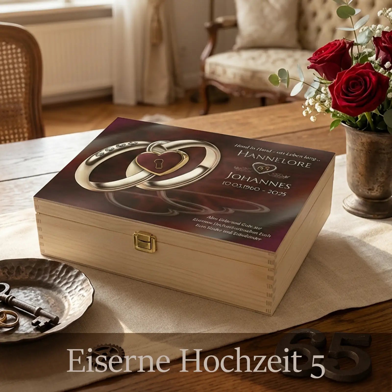 Personalisierte Holzbox zur Eisernen Hochzeit mit hellem Holz und Metallverschluss. Der Deckel zeigt zwei ineinander verschlungene Eheringe mit Herzsymbol sowie die Namen Hannelore und Johannes mit Jubiläumsdatum. Die Box steht auf einem gedeckten Tisch mit Stoffläufer, Schlüssel, Kerzenlicht und Rosen und steht symbolisch für 65 Jahre Ehe und gemeinsame Geschichte.