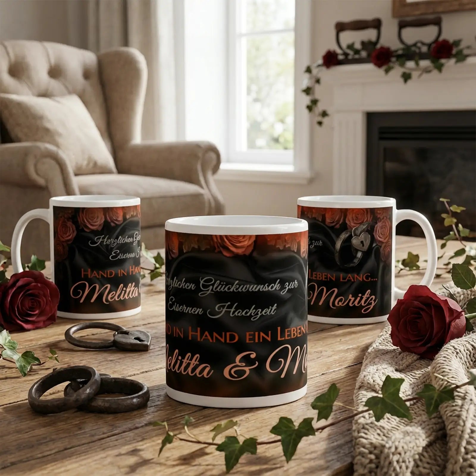 Personalisierte Motivtassen zur Eisernen Hochzeit mit Namen Melitta und Moritz, schwarzes Design mit roten Rosen, Handschrift-Schriftzug, eiserne Ringe auf Holztisch, Wohnzimmerambiente mit Sessel, Kamin und warmem Licht