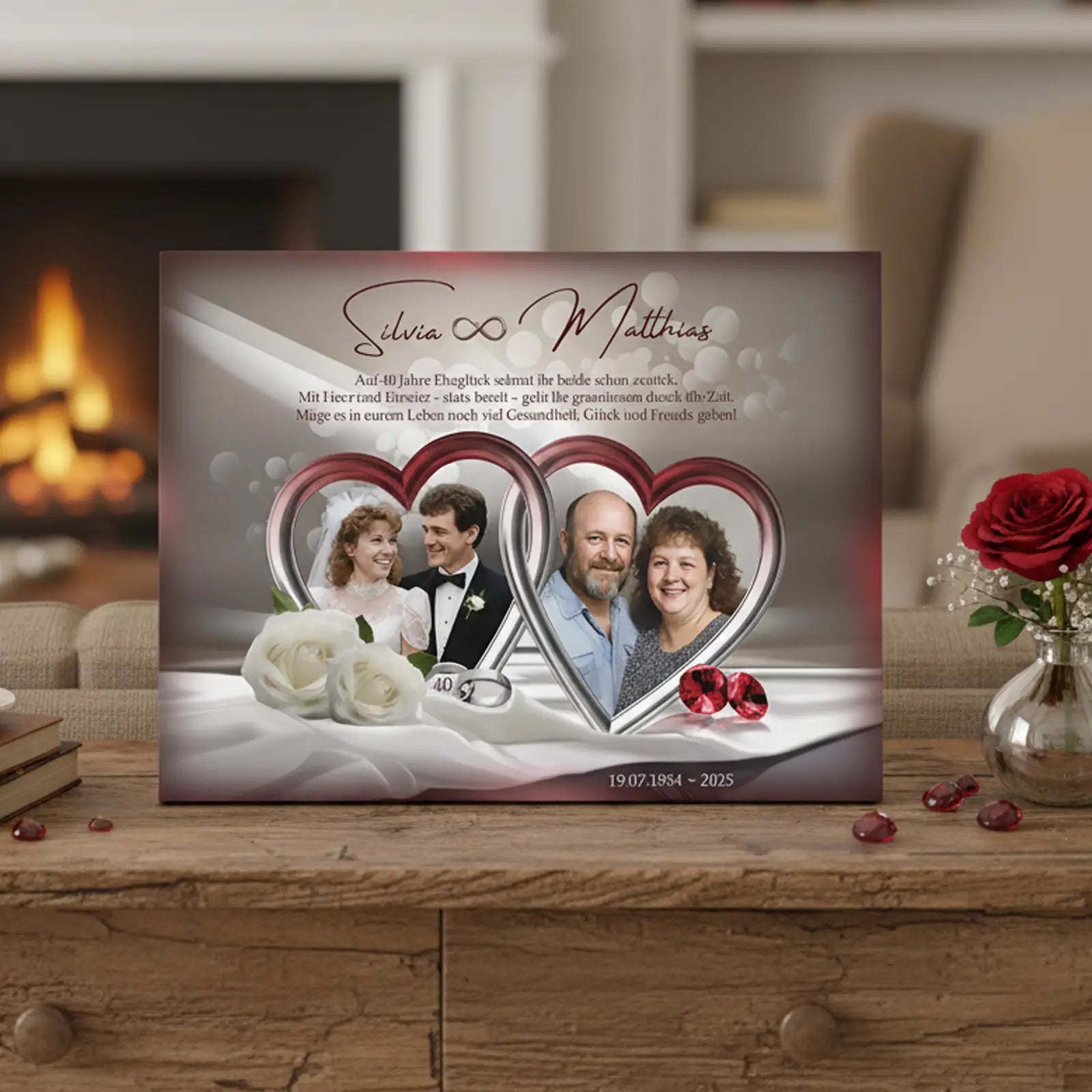 Personalisierte Fotoleinwand zur Rubinhochzeit (40 Jahre) mit zwei Fotos eines Ehepaares in herzförmigen Rahmen: links das Hochzeitsfoto aus jungen Jahren, rechts das Paar im heutigen Alter. Auf der Leinwand stehen die Namen Silvia und Matthias, ein Glückwunschtext zum 40. Hochzeitstag sowie das Datum 19.07.1985–2025. Dekorative Elemente sind weiße Rosen, rote Schmucksteine und ein heller Stoffhintergrund. Die Leinwand steht auf einem Holztisch in einem Wohnzimmer mit Kamin im Hintergrund.