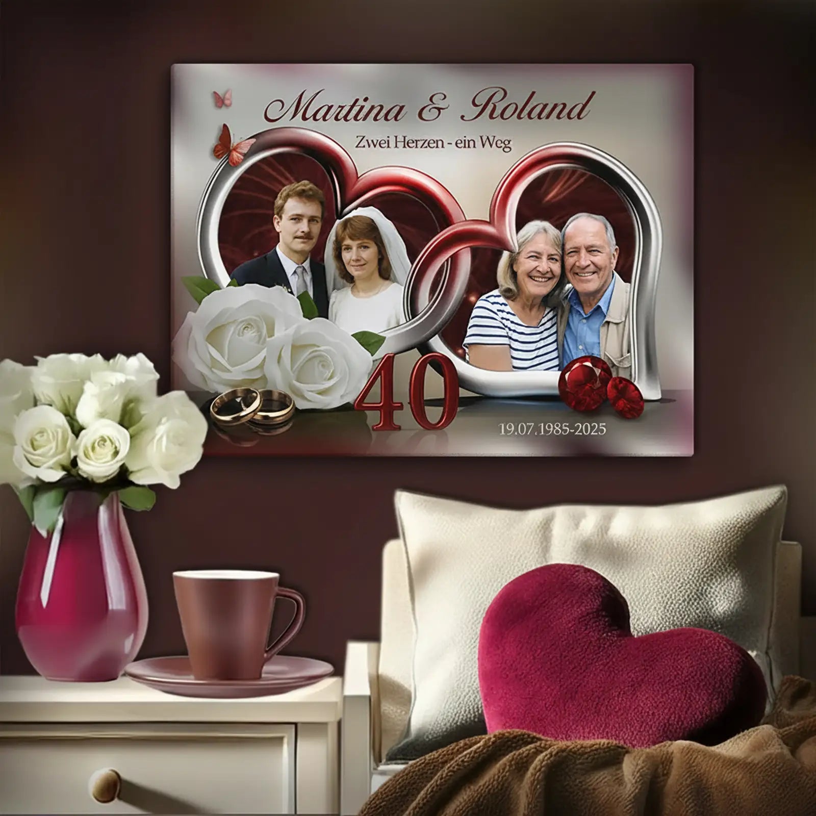 Personalisierte Fotoleinwand zur Rubinhochzeit (40 Jahre Ehe), aufgehängt über einem Nachttisch in einem gemütlichen Schlafzimmer. Die Leinwand zeigt zwei Paarfotos von Martina und Roland: links das Ehepaar an ihrem Hochzeitstag, rechts das Paar im heutigen Alter. Die Fotos sind in zwei roten Herzrahmen gestaltet. Darunter stehen zwei goldene Eheringe, die Zahl 40 in Rot sowie die Jahreszahlen 19.07.1985–2025. Neben der Leinwand stehen eine Vase mit weißen Rosen und eine Kaffeetasse; im Vordergrund liegt ei
