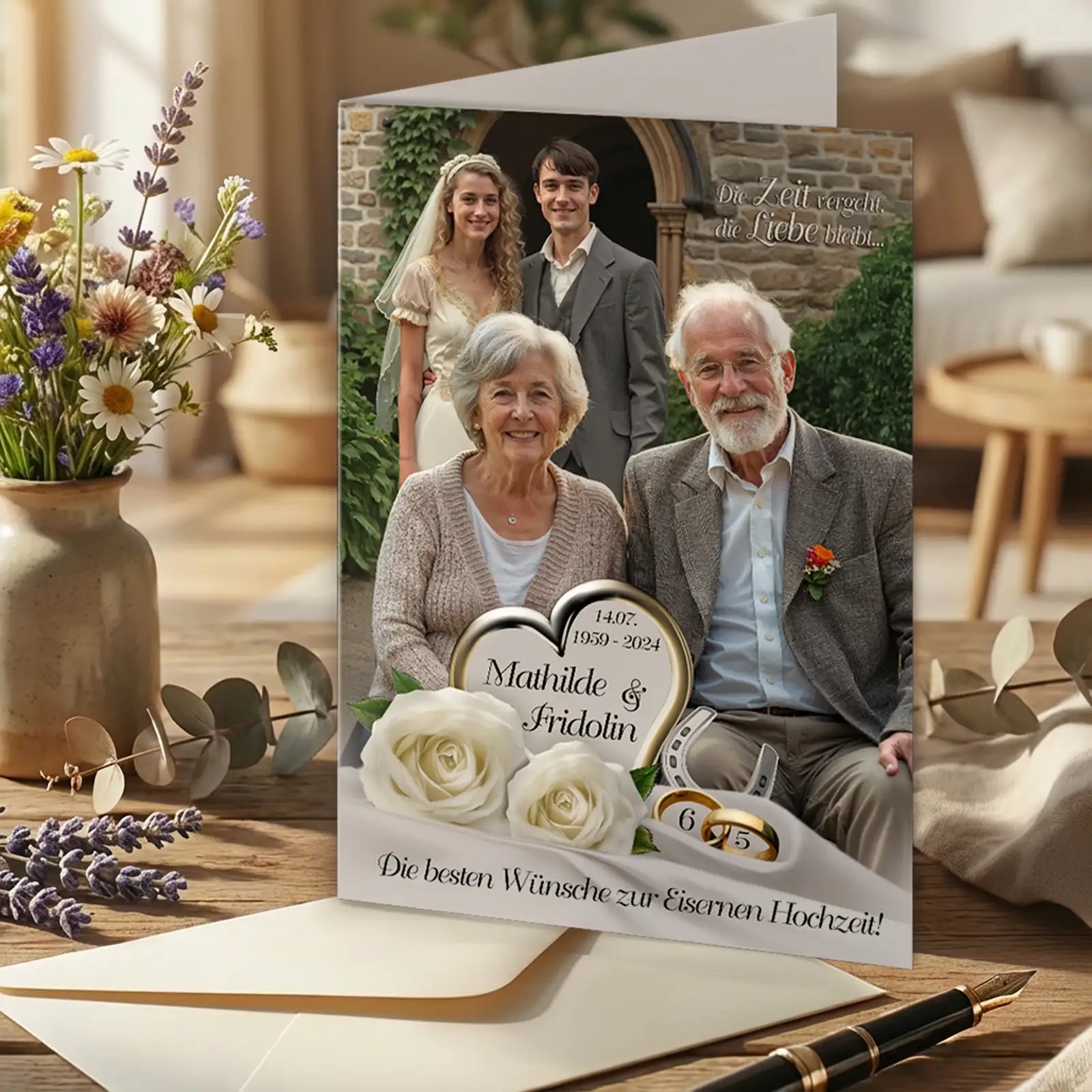 Personalisierte Glückwunschkarte zur Eisernen Hochzeit mit Familienfoto, älteres Ehepaar Mathilde und Fridolin im Vordergrund, jüngeres Paar im Hintergrund vor Steinbogen, Herzmotiv mit Namen und Jahreszahlen 1959–2024, Zahl 65, weiße Rosen und Eheringe, Hochzeitsspruch „Die besten Wünsche zur Eisernen Hochzeit“, liebevoll arrangierte Tischszene mit Blumen, Umschlag und Füllfederhalter.