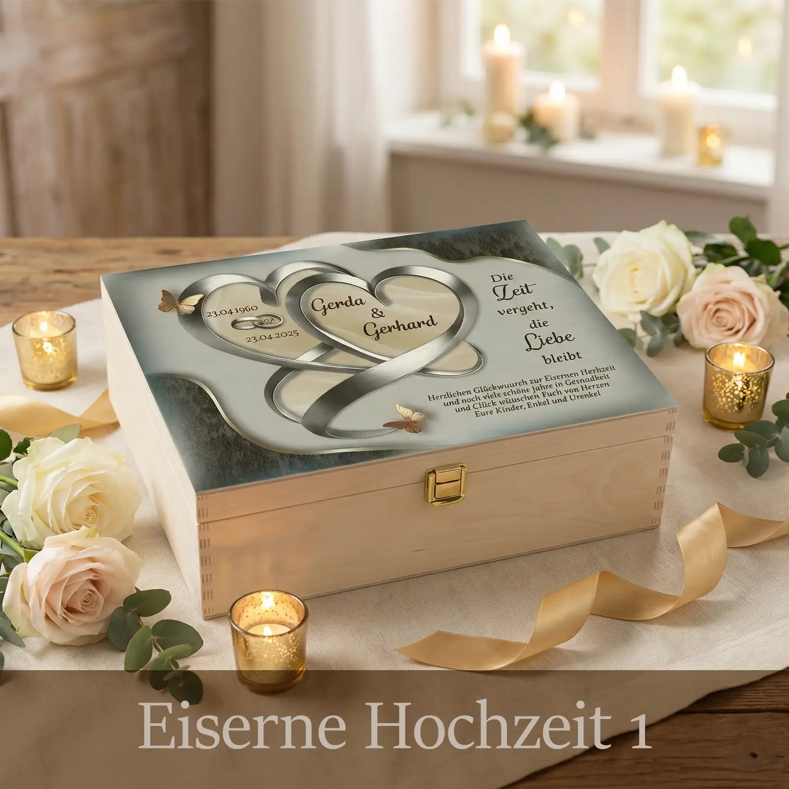 Personalisierte Holzbox zur Eisernen Hochzeit mit hellem Holz und Metallverschluss. Auf dem Deckel sind zwei ineinander verschlungene silberne Herzen als Unendlichkeitsband mit den Namen Gerda und Gerhard sowie Jubiläumsdaten abgebildet. Goldene Schmetterlinge setzen feine Akzente. Die Box steht dekoriert mit Kerzen, Rosen und Stoffband auf einem festlich gedeckten Tisch und wirkt edel, ruhig und zeitlos.