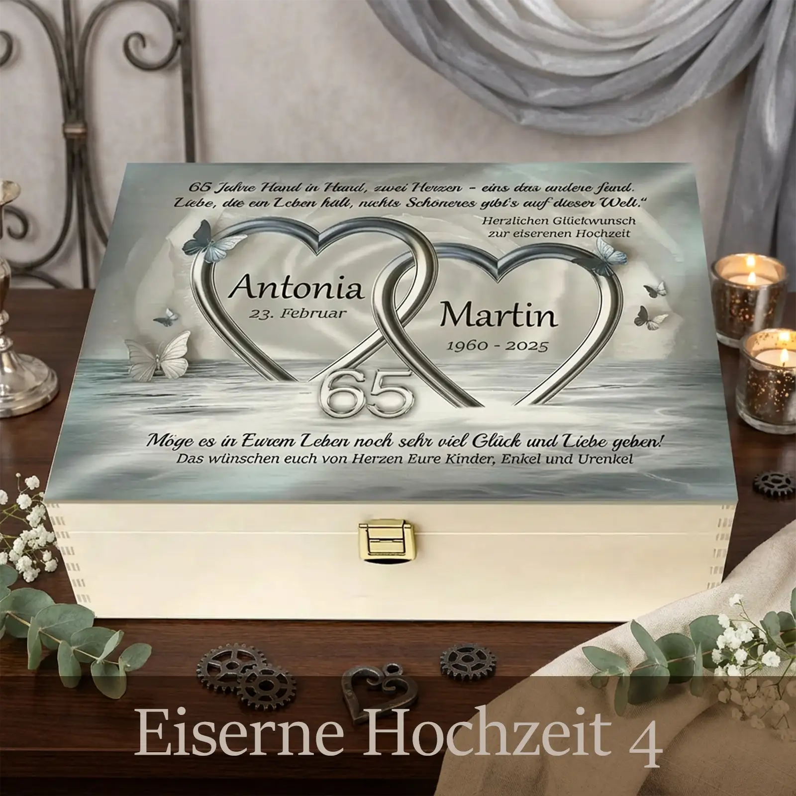 Personalisierte Holzbox zur Eisernen Hochzeit mit hellem Holz und Metallverschluss. Auf dem Deckel sind zwei ineinander verschlungene Herzen mit der Zahl 65 sowie die Namen Antonia und Martin mit Jubiläumsdaten gestaltet. Die Box steht auf einer festlich dekorierten Oberfläche mit Kerzen, Stoffen und floralen Elementen und symbolisiert 65 Jahre Ehe und Verbundenheit.