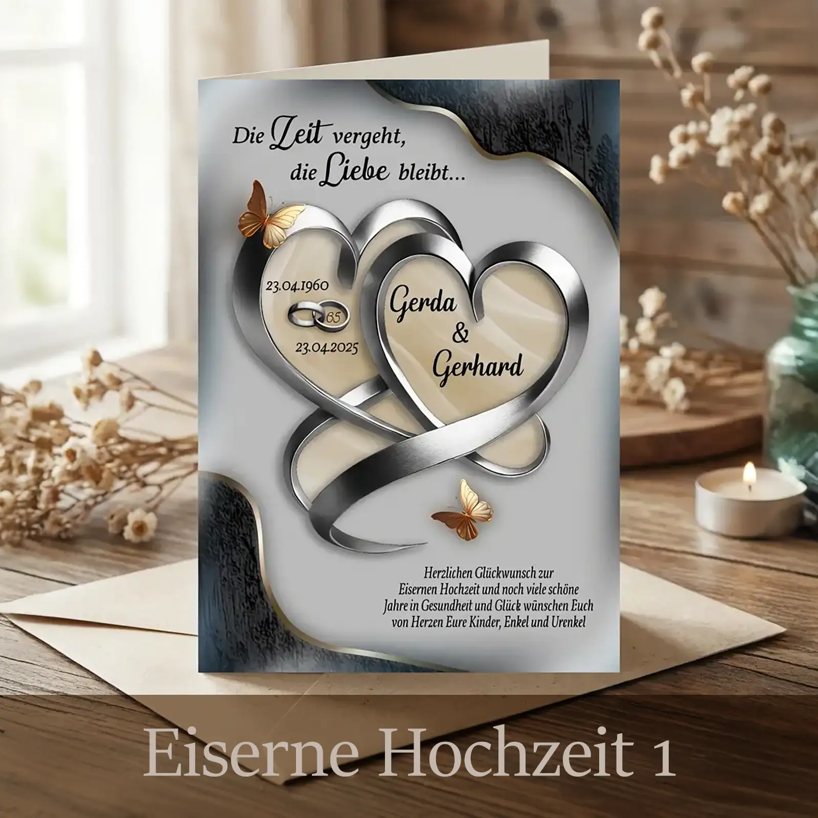 Personalisierte Glückwunschkarte zur Eisernen Hochzeit in hellem Silber-Beige: Zwei ineinander verschlungene metallische Herzen bilden ein Unendlichkeitsband und tragen die Namen Gerda und Gerhard mit Jubiläumsdaten. Goldene Schmetterlinge setzen Akzente. Die Karte steht auf einem Holztisch vor Umschlag, Kerze und Trockenblumen und wirkt ruhig, wertig und zeitlos.